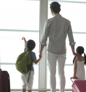 family with suitcases facing away looking out a window