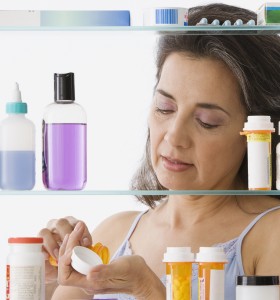 Hispanic woman measuring out medicine in front of a medicine cabinet