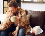 Man wrapped in a blanket blowing his nose.