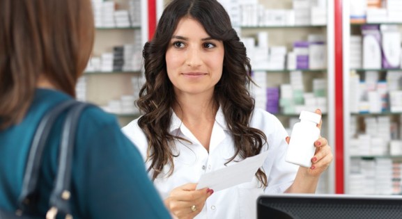 Pharmacist with long dark hair assisting customer in dark green shirt